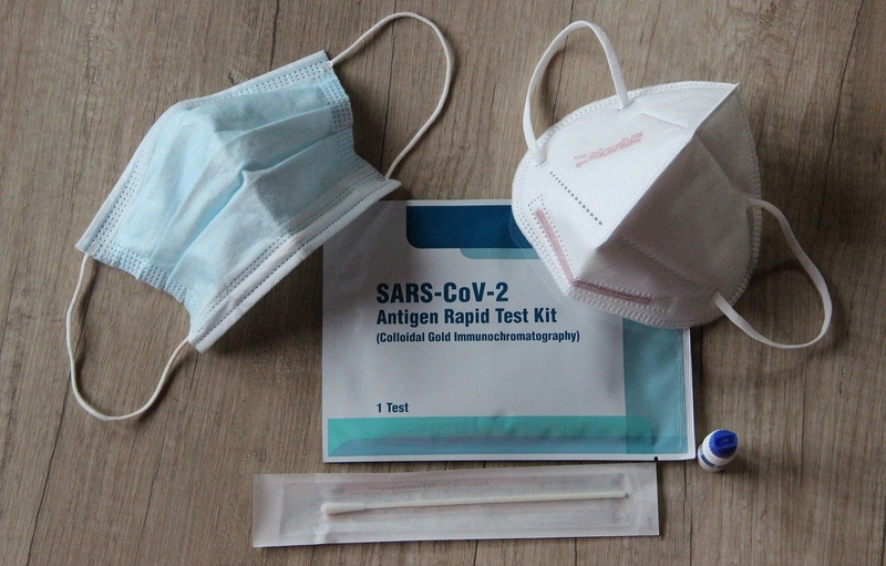 Corona Schnelltest-Kit flankiert von OP-Maske oben links und FFP2-Maske oben rechts